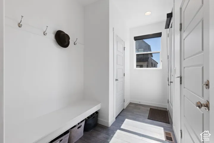 Built-in bench with storage, wall-mounted coat hooks, wood-finish flooring, recessed lighting, and a white interior door