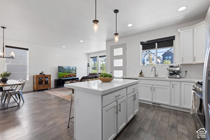 Well-appointed kitchen featuring white cabinetry, a center island with a light-toned countertop, a stainless steel sink, and a subway tile backsplash