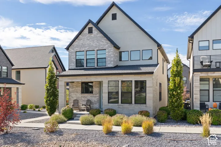 Contemporary exterior with light brick and stucco finishes, a covered front porch, a dark shingle roof, and dark-framed windows