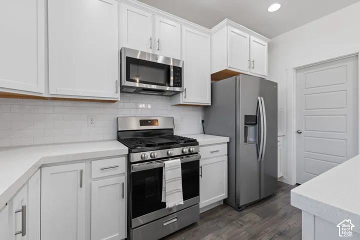 White shaker cabinetry, stainless steel appliances, white subway tile backsplash, light-toned countertops, and wood-finish flooring