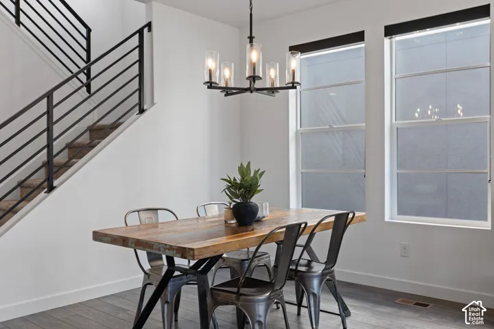 Modern chandelier with clear glass shades, wood-finish flooring, two large windows with roller shades, and a staircase featuring black metal railings