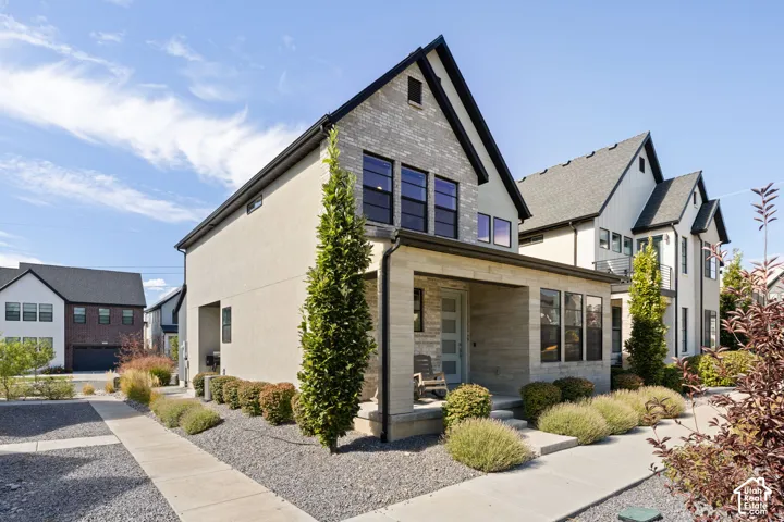 Contemporary architecture featuring a multi-textured facade, gabled roofline, covered entry, and expansive front windows