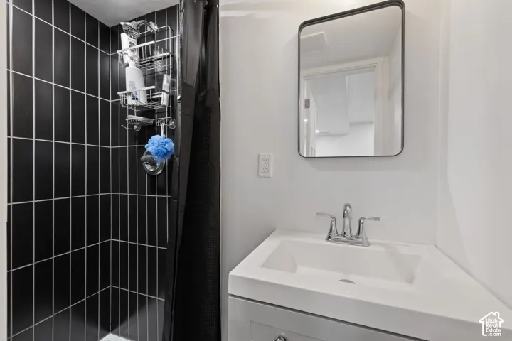 Black subway tile shower surround with white grout, single vanity with integrated sink, chrome faucet, and rectangular framed mirror