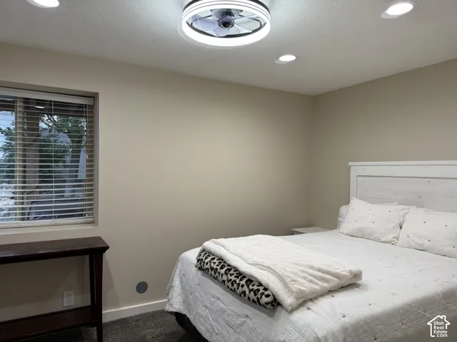 Recessed ceiling lighting, ceiling-mounted fan fixture, window with blinds, and white panel headboard