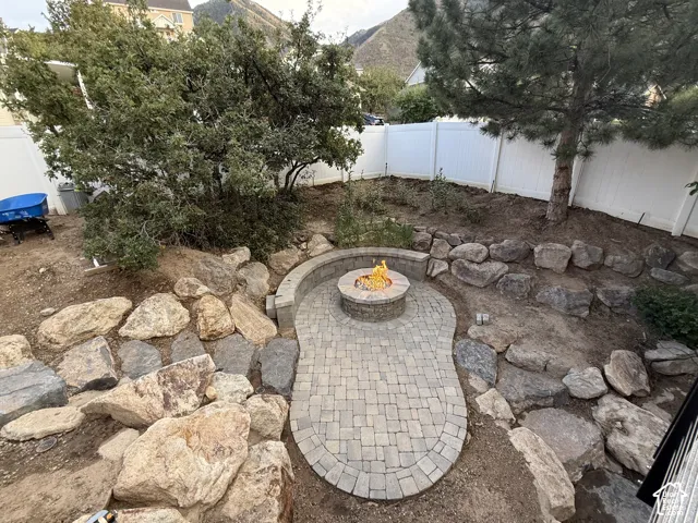 Paver patio with an integrated fire pit, stone retaining walls, privacy fencing, and established trees