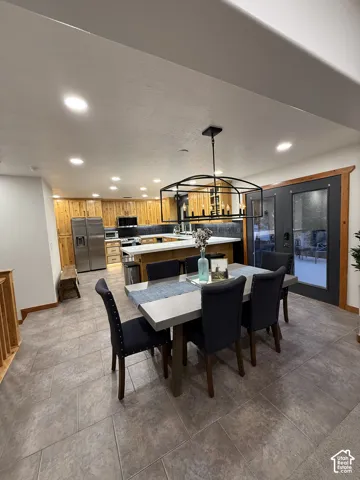Spacious dining area featuring a modern chandelier, adjacent to a kitchen with wood cabinetry and stainless steel appliances