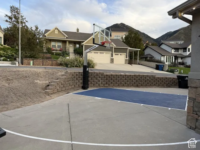 Paved court with blue playing surface, stone retaining wall with integrated steps, and mountain backdrop