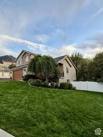 Front exterior featuring a stone and stucco facade, an attached garage with a wood-finish door, a front lawn, and a white privacy fence