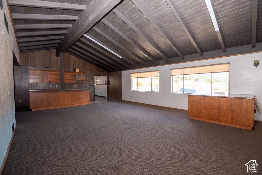 Vaulted ceiling with exposed beams, wood-paneled walls, built-in wood cabinetry, and multiple windows