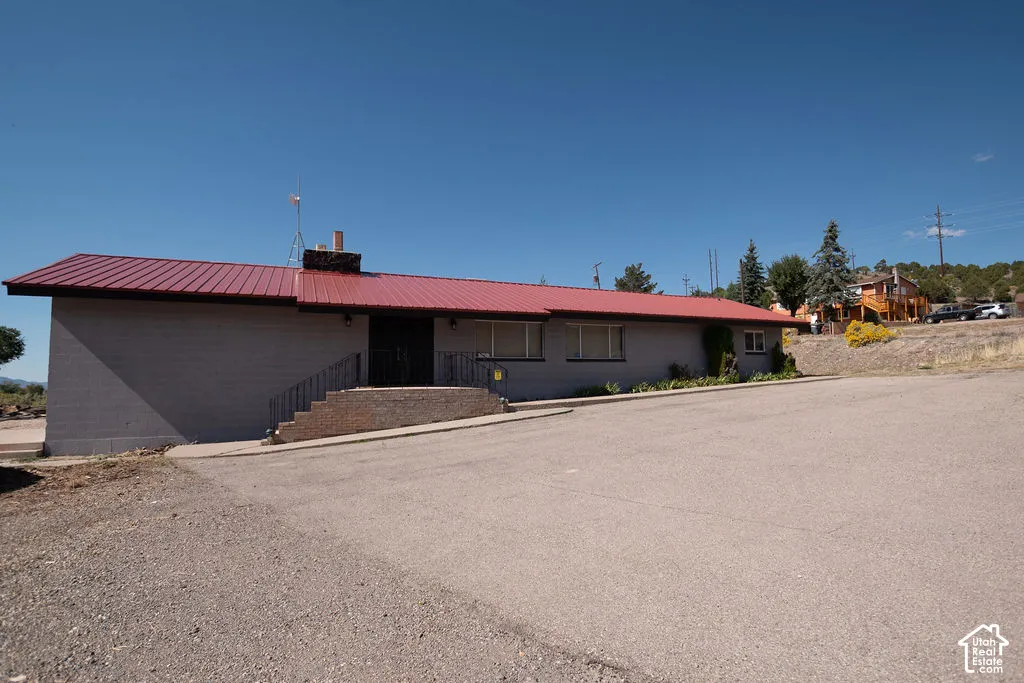 Exterior featuring a red metal roof, light-colored block siding, a paved entry, and a stone-clad chimney