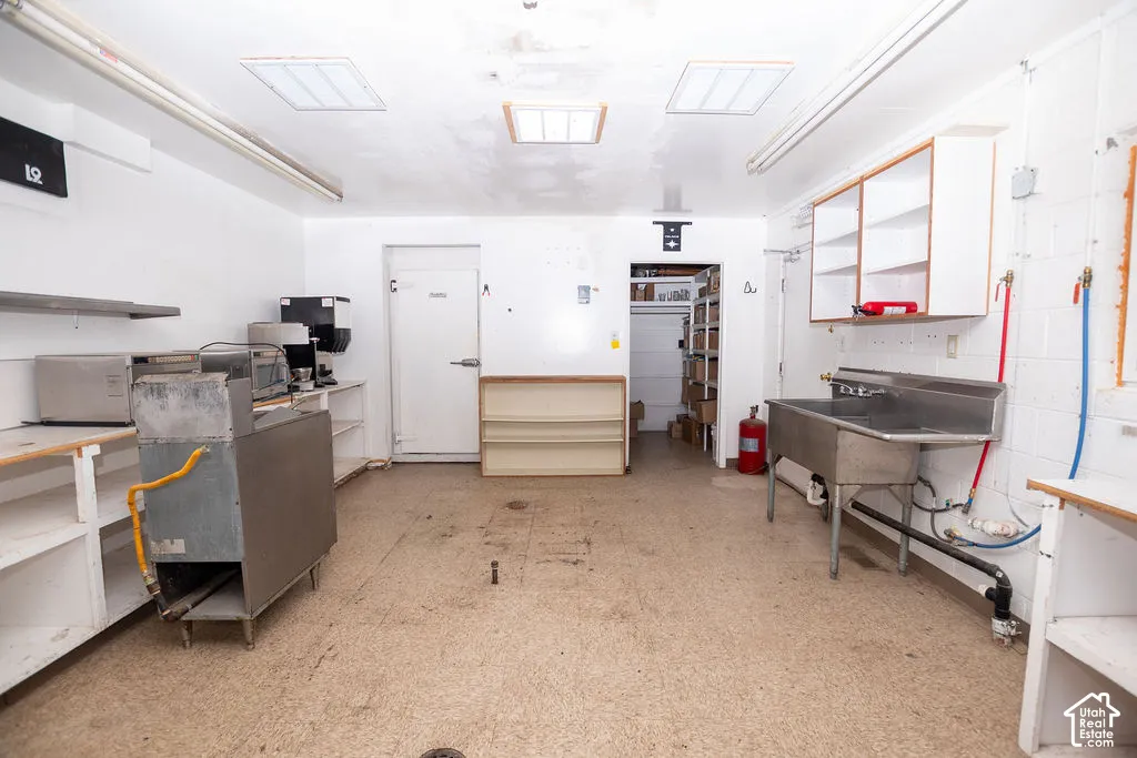 Commercial-grade stainless steel sink, built-in shelving, white upper cabinetry, and commercial flooring