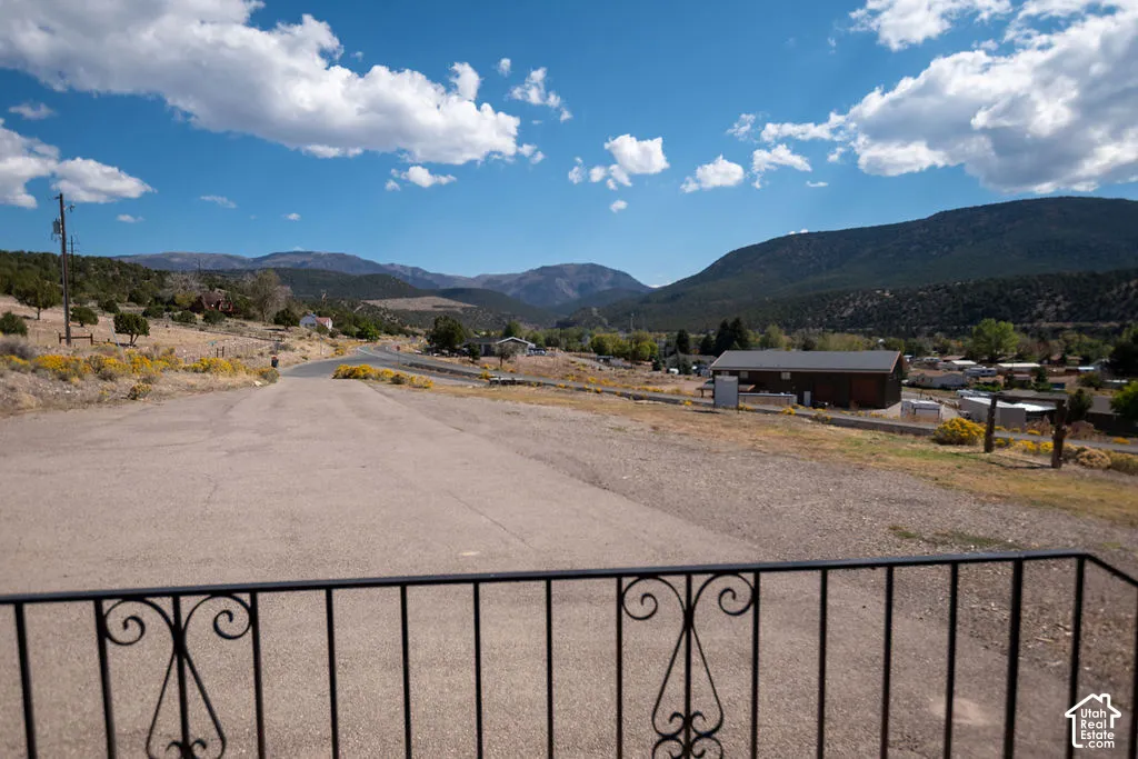 Wrought iron railing overlooking a paved surface, distant mountains, and scattered trees