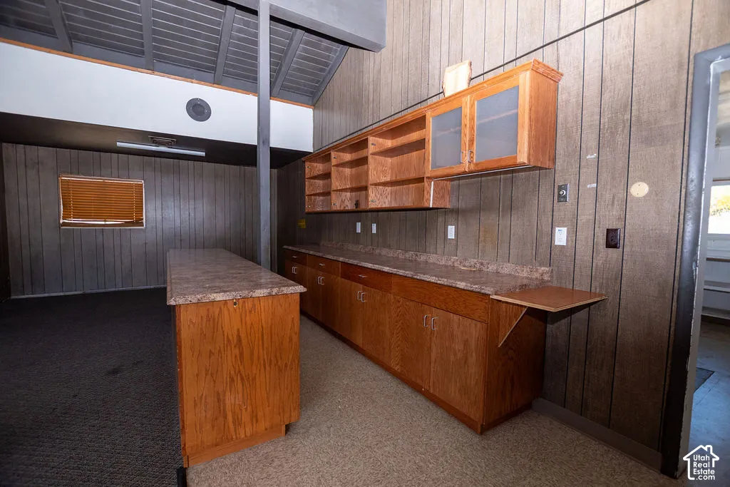 Wood-finish cabinetry and countertops, vertical wood-panel wall treatment, and an exposed beam ceiling