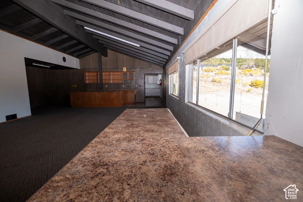 Vaulted ceilings with exposed beams, wood-paneled walls, built-in cabinetry, and integrated bar area