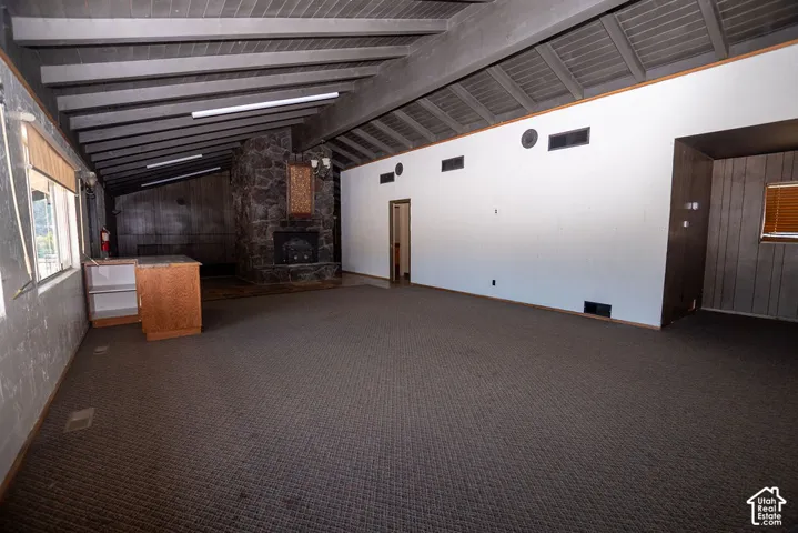 Spacious room featuring a stone fireplace, exposed beam ceiling, and durable carpet flooring