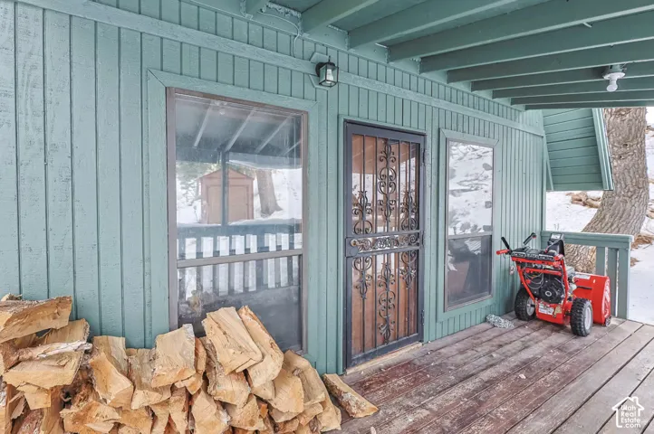 Board-and-batten siding with a covered wood deck, featuring an ornate security screen door and exterior lighting fixtures