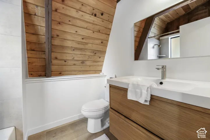 Wood-plank wall accent, rectangular vanity mirror, wood-finish vanity with integrated sink, contemporary faucet, and wood-finish flooring