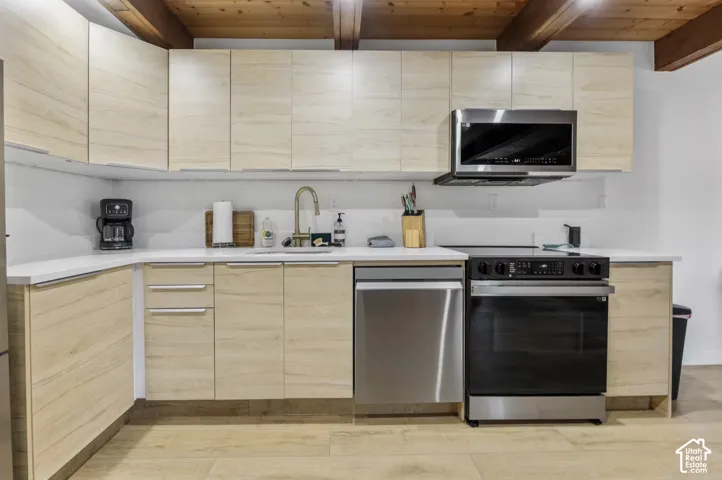 Light wood-finish cabinetry with white countertops, stainless steel appliances, and a gold-finish faucet