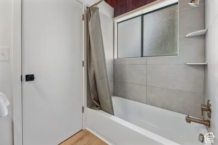 White bathtub with brushed nickel fixtures, light gray tile surround, and built-in shelves