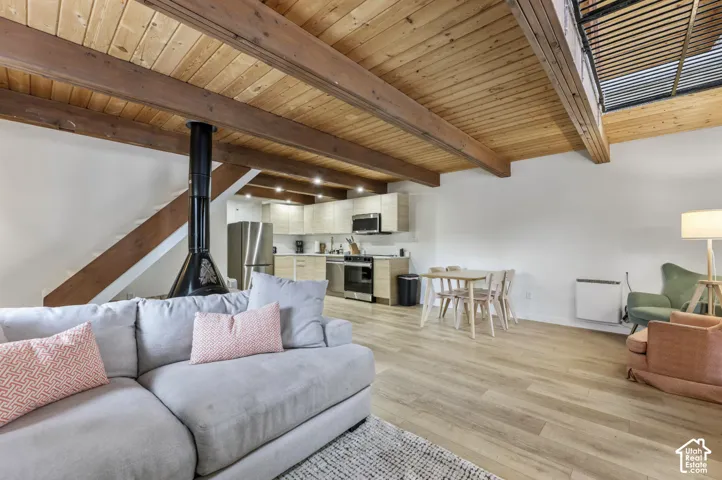 Vaulted wood-finish ceilings with exposed beams, wood-finish flooring, a built-in fireplace, and a kitchen featuring stainless steel appliances