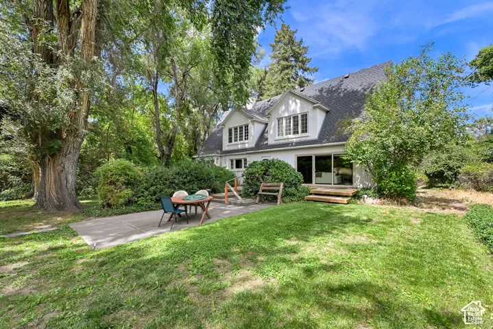 White stucco exterior with a dark shingle roof, dormer windows, and a concrete patio