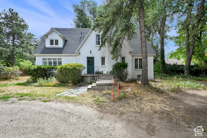 White stucco exterior with a dark shingle roof, featuring a dormer window and multiple pane windows