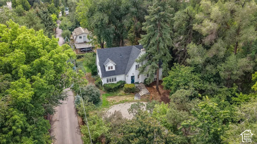 White exterior with dark roof and dormer windows, surrounded by mature trees
