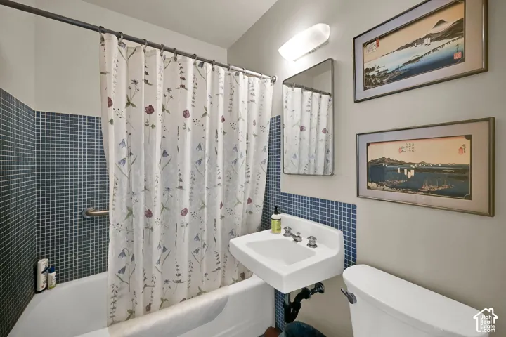 Tub/shower combination with blue mosaic tile surround, wall-mounted sink with chrome fixtures, and a toilet