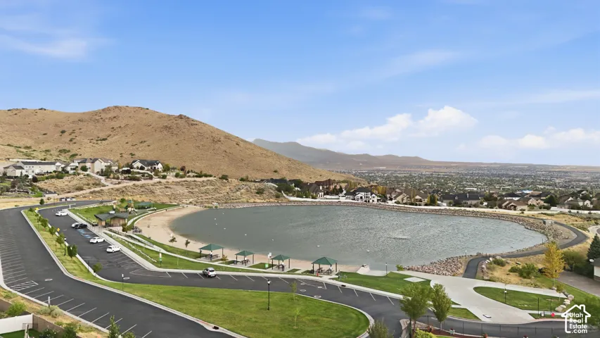 Community lake with sandy beach, adjacent paved walking path, surrounding residential properties, and distant city landscape
