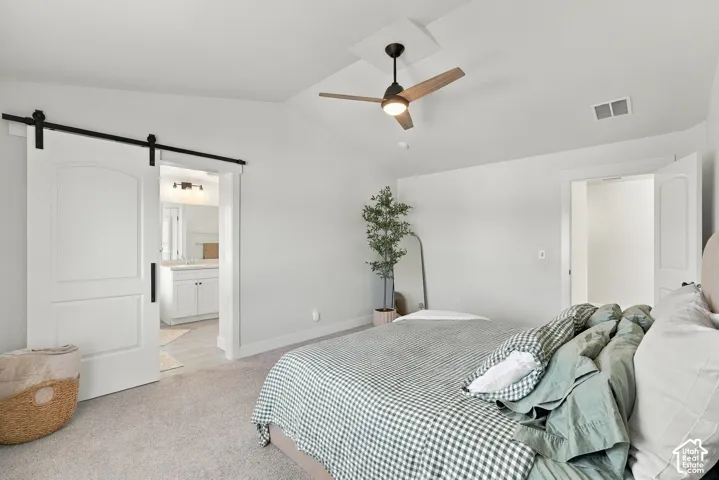 Vaulted ceiling with an integrated ceiling fan, light-toned carpet flooring, white barn door entry, and a dual-sink vanity with a large mirror