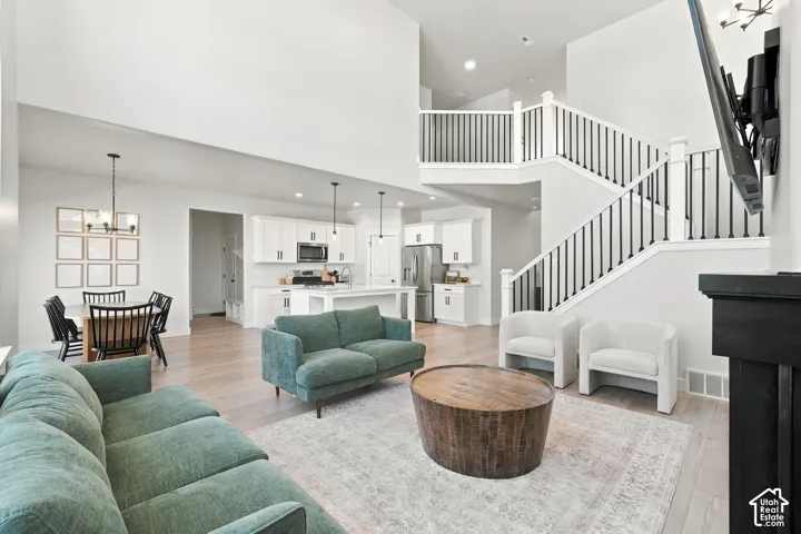 Open-concept living space featuring high ceilings, wood-finish flooring, a contemporary staircase with dark metal balusters, a kitchen with white cabinetry, and a dining area with a modern chandelier
