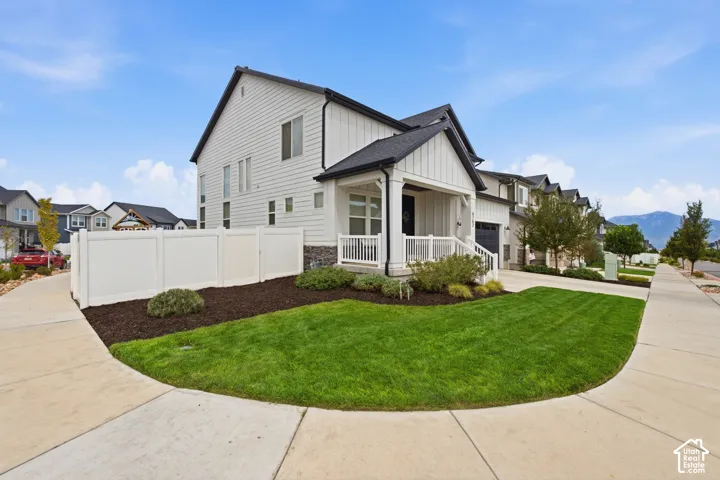 White exterior siding with dark trim, covered front porch, integrated garage, and a manicured lawn