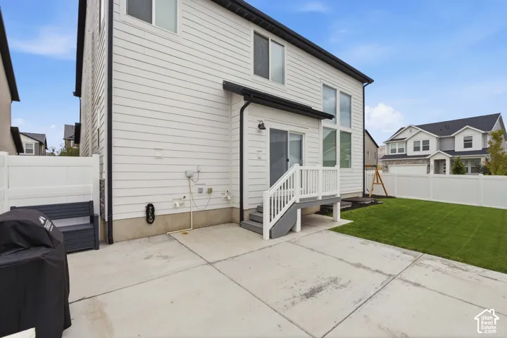 Exterior featuring white horizontal siding, a concrete patio, a grass lawn, white vinyl fencing, and a rear deck with steps