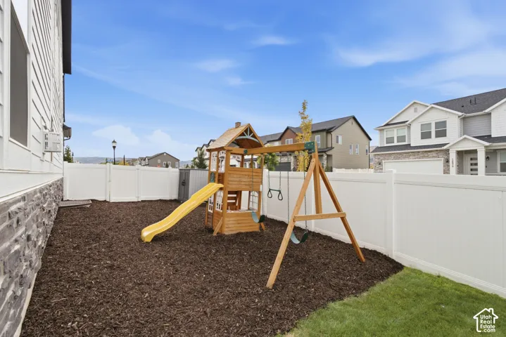 Fully fenced side yard with wood playground structure, slide, and swings