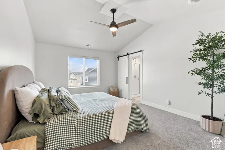 Vaulted ceiling with a ceiling fan, carpeted flooring, window with blinds, and a barn door entry