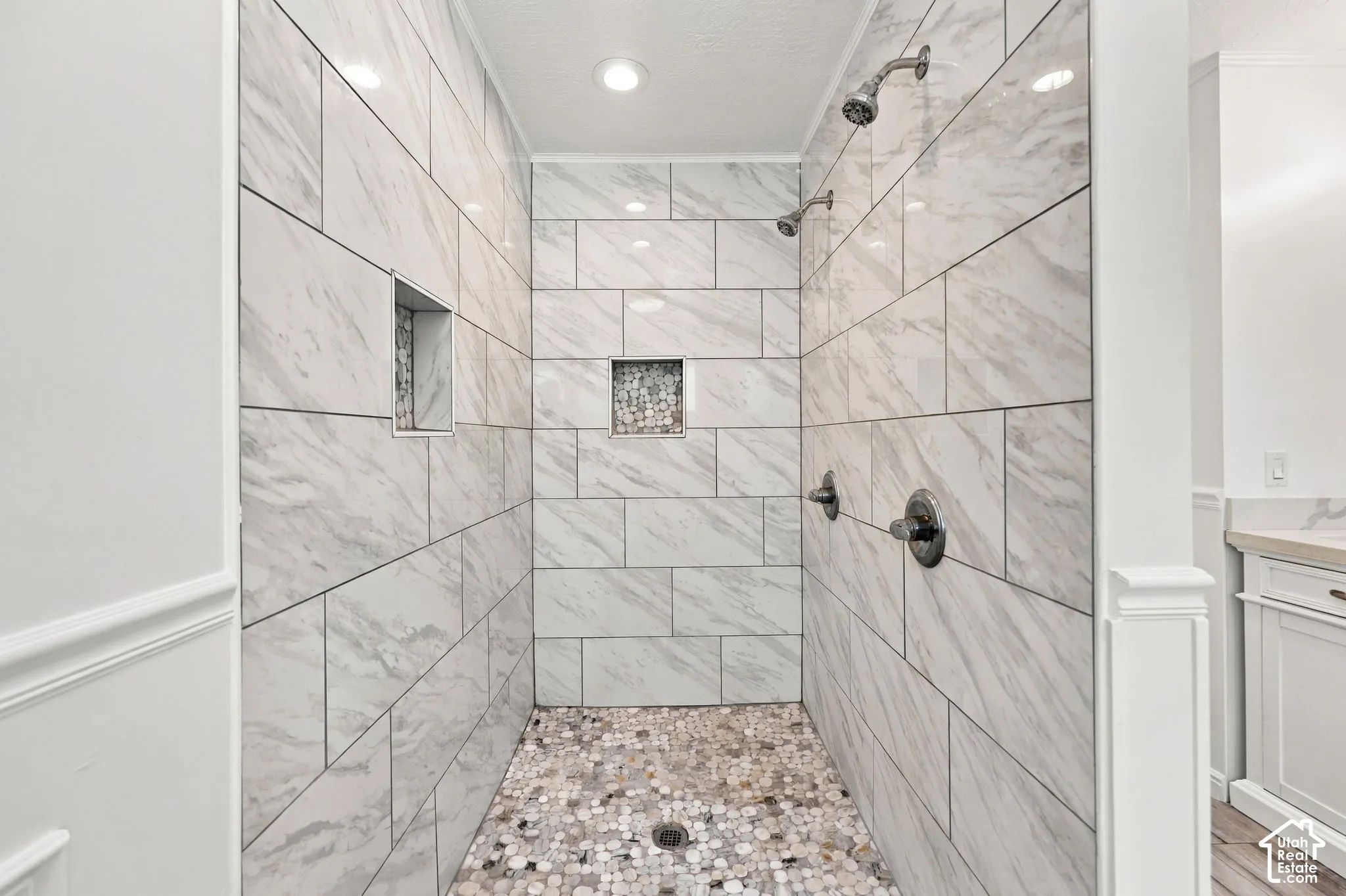 Spacious shower with large format tile, pebble shower floor, built-in shower niches, and dual shower heads