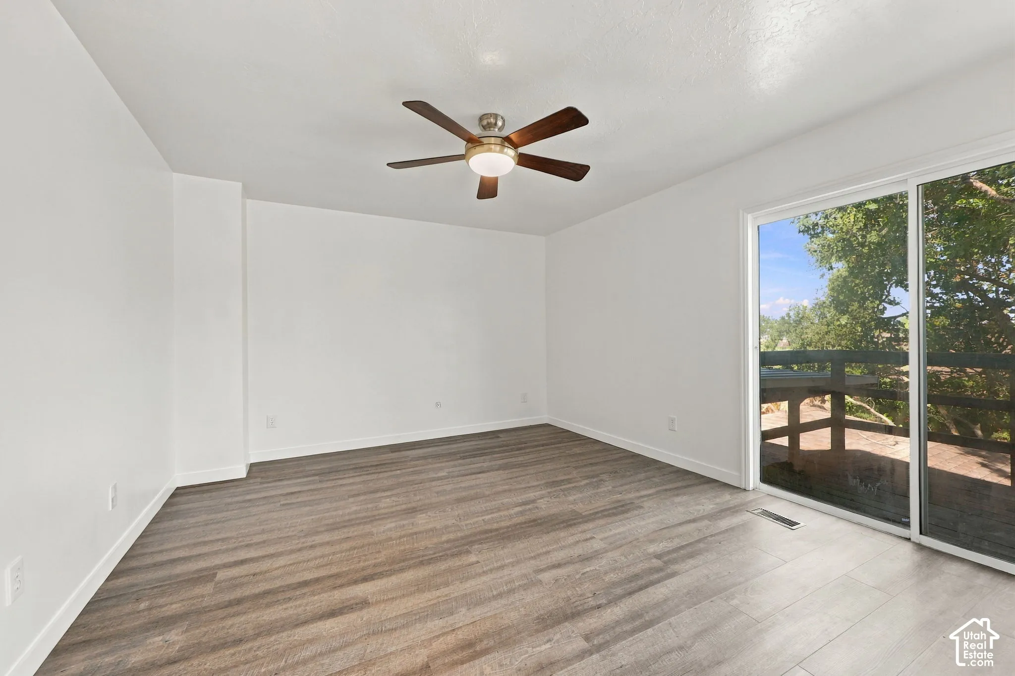 Wood-finish flooring with white baseboards, a ceiling fan with light, and a sliding glass door providing exterior access