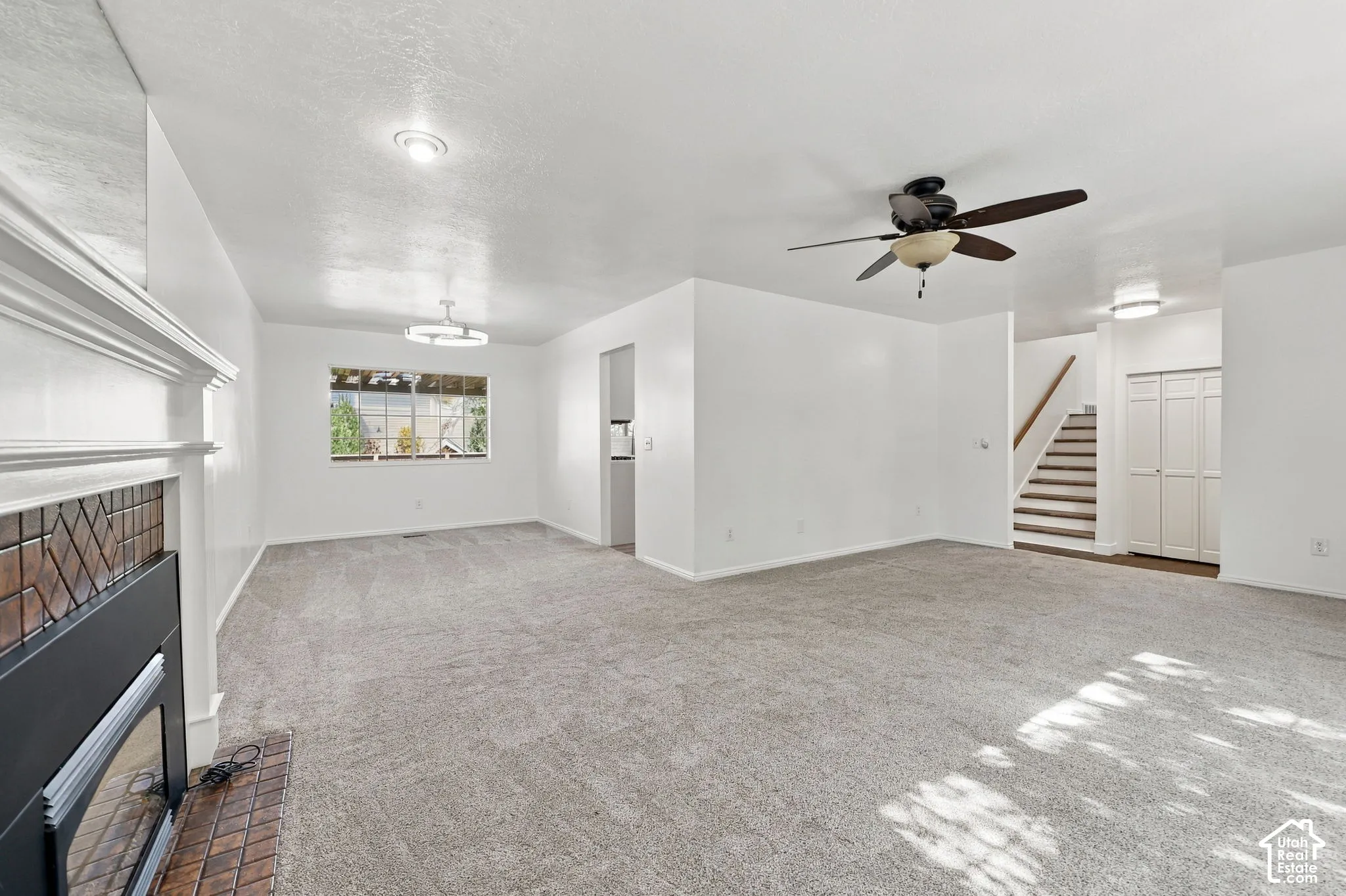 Carpeted living area featuring a fireplace with a decorative tile surround and mantel, a ceiling fan, and a window with outdoor scenery