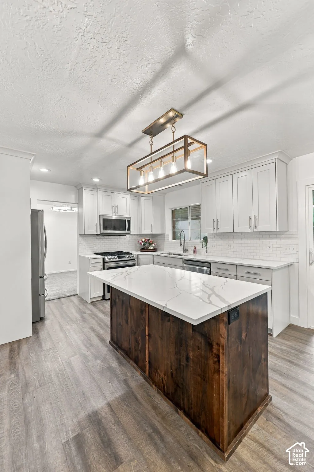 Kitchen featuring wood-finish flooring, white cabinetry, a white subway tile backsplash, a center island with a white countertop and wood paneling, and stainless steel appliances