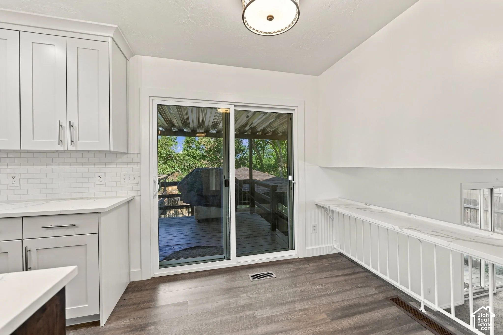 White shaker cabinetry with brushed nickel hardware, white subway tile backsplash, white countertop, wood-finish flooring, and a sliding glass door