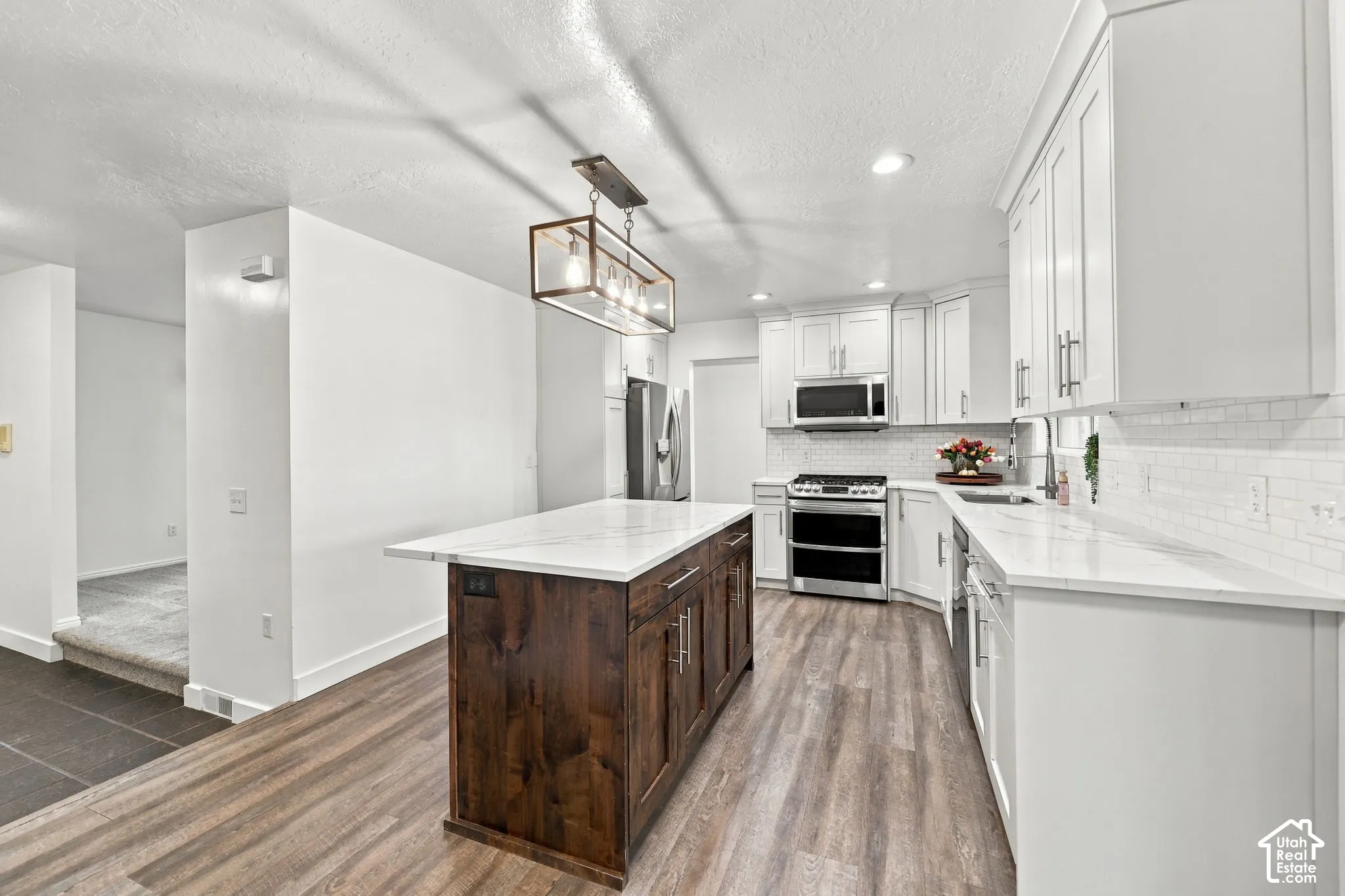 Kitchen featuring white cabinetry, stainless steel appliances, white subway tile backsplash, a wood-finish island with a white countertop, and wood-finish flooring