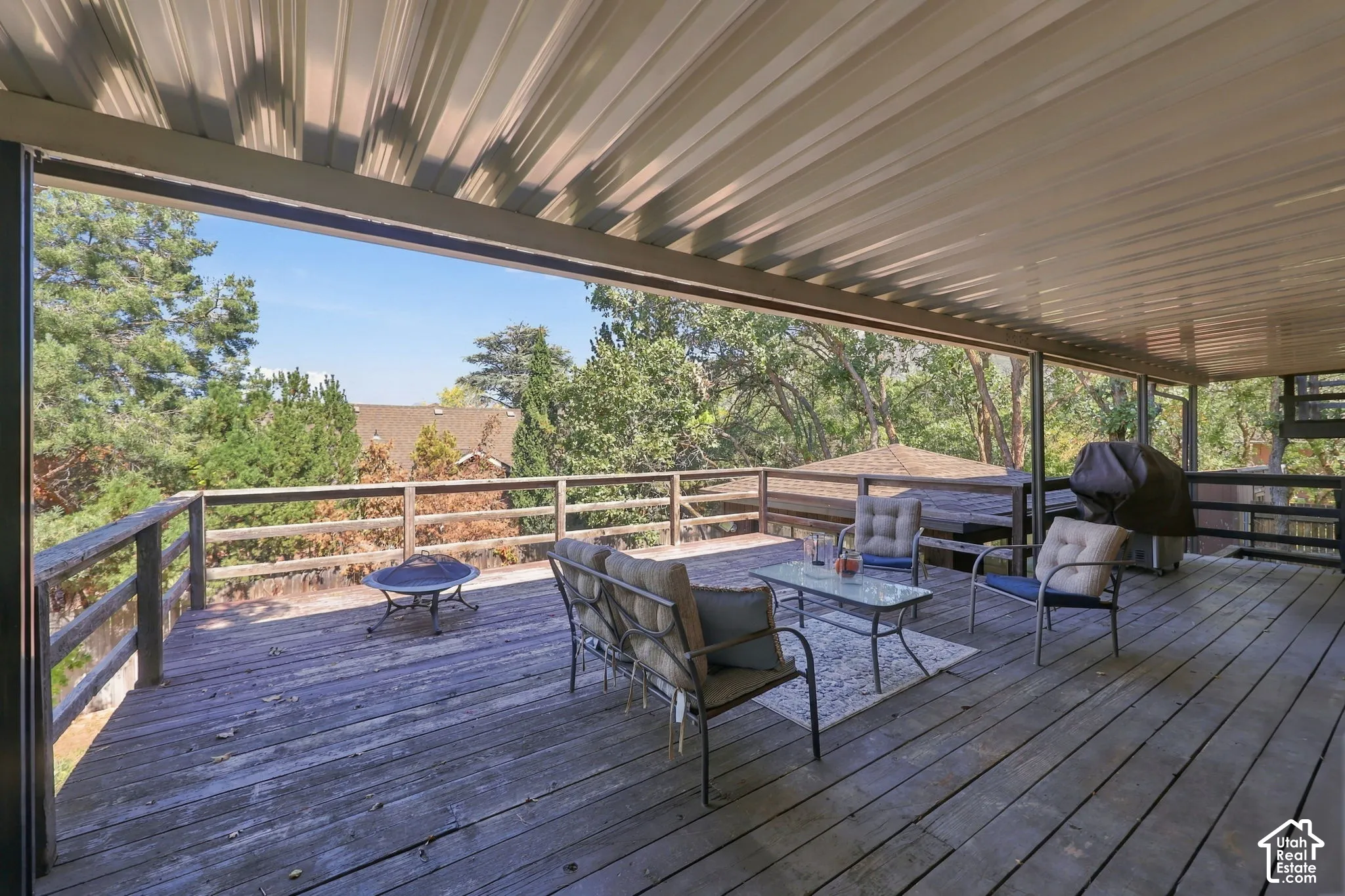 Expansive wood deck with a full-length covered patio, wood railings, and mature landscaping