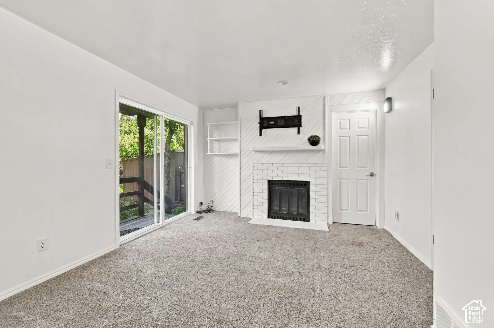 White brick fireplace with mantel, built-in shelving, sliding glass door, and neutral-toned carpeting
