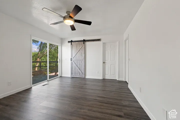 Wood-finish flooring, white painted walls, sliding glass door, a contemporary ceiling fan, and a barn door