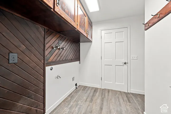 Laminate wood-finish flooring, white paneled door, wood paneled walls, wood upper cabinetry, and a wood coat rack