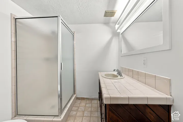 Frosted glass shower enclosure, wood-finish vanity with tile countertop, integrated basin, and chrome-finish faucet