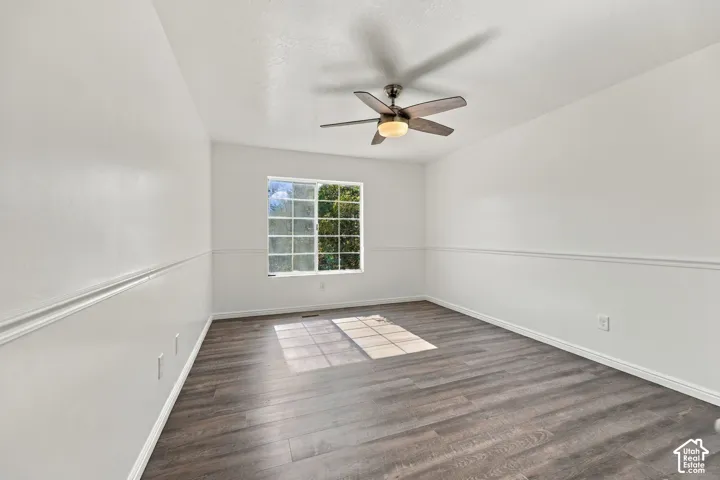 Wood-finish flooring, white walls with chair rail molding, ceiling fan with integrated lighting, and a multi-pane window