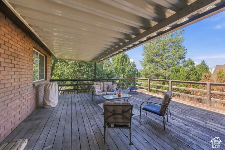 Expansive wood-finish deck with a solid overhead covering, featuring a natural wood railing and a brick exterior wall