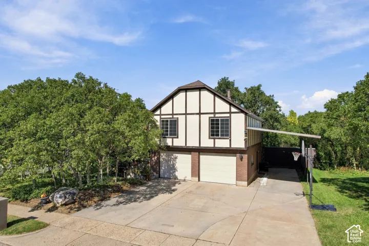 Tudor-style exterior with decorative half-timbering, dual garages with light-toned doors, brick detailing on the lower level, and mature trees on the property
