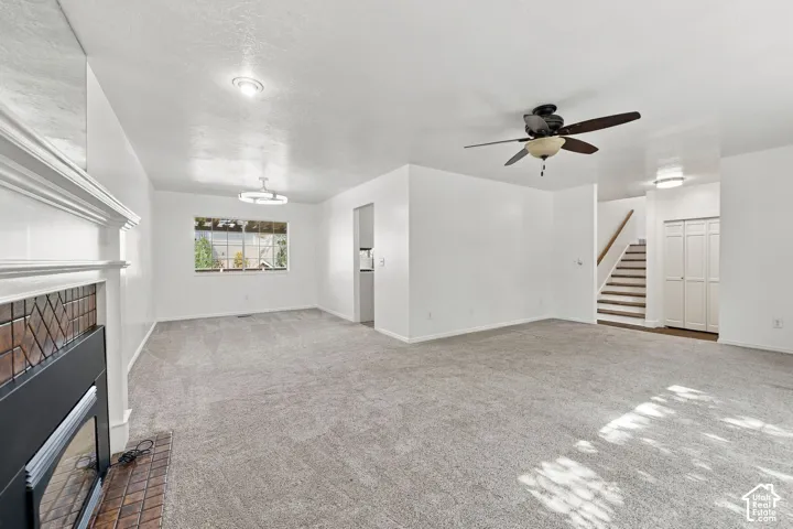 Carpeted living area featuring a fireplace with a decorative tile surround and mantel, a ceiling fan, and a window with outdoor scenery